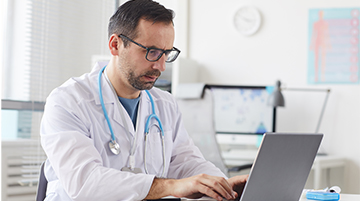 Doctor reviewing patient records on a laptop in an exam room