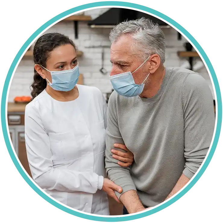Caregiver supporting an elderly man wearing face masks during a home visit, assisting him